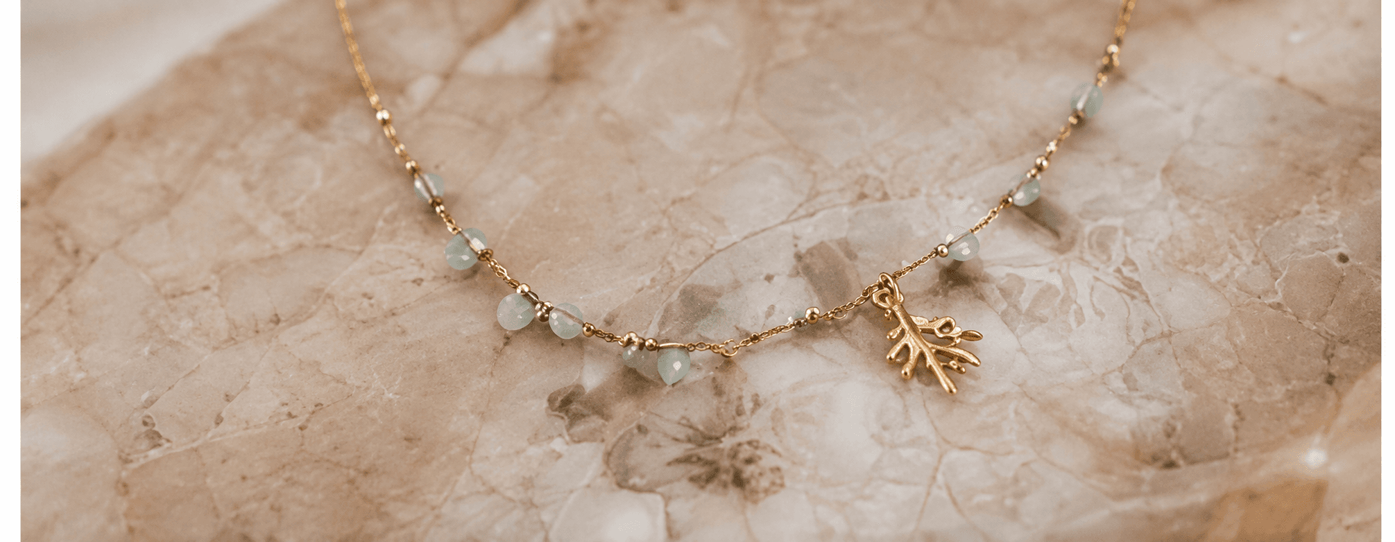 A fine gold chain strung with small green beads and a leaf charm, on pale fabric