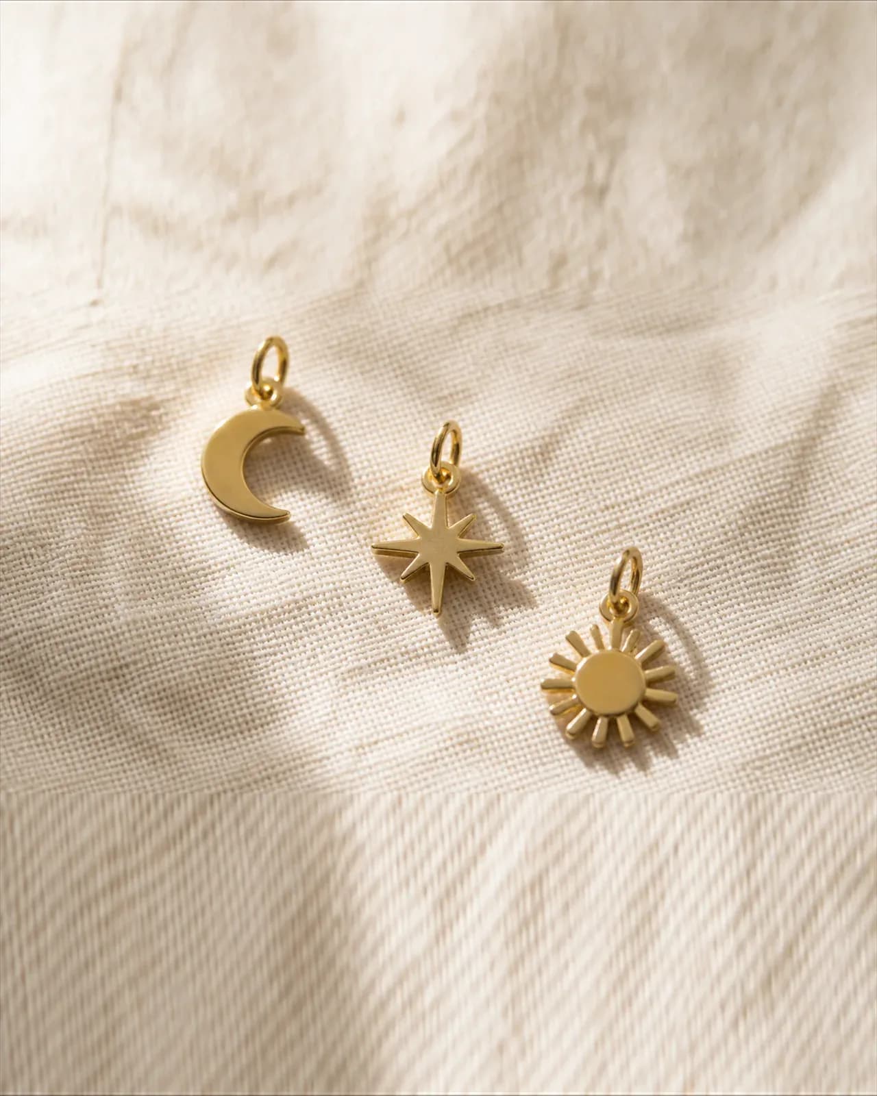 Three small flat gold charms on ivory linen